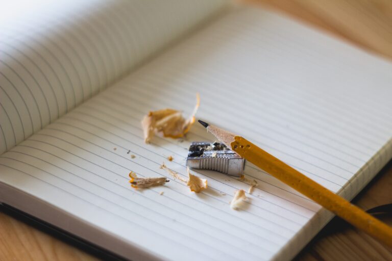 A pencil, sharpener and sharpenings from the pencil sitting on a blank page of a notebook